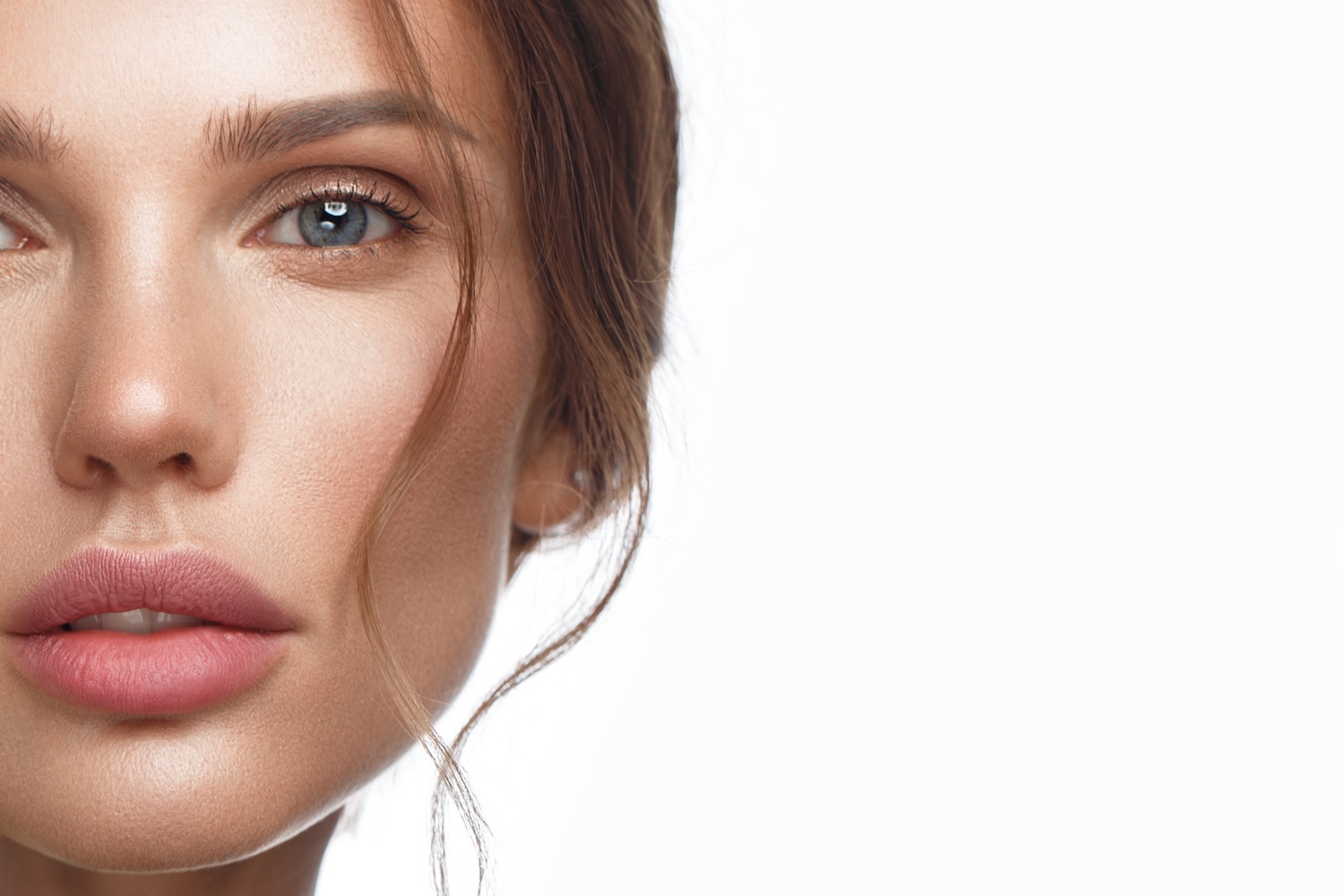 close-up of a woman’s face showing smooth skin, one eye visible, and loose hair against a white background