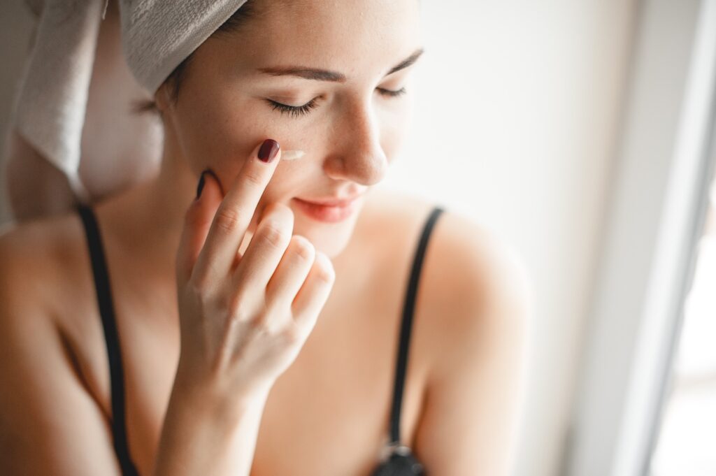 woman applying a small amount of cream to her cheek with her finger