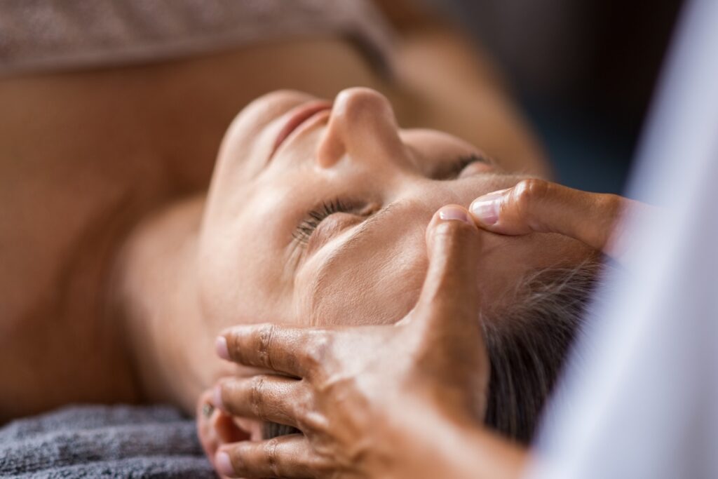 person lying down with eyes closed while hands gently massage the face near the temples and forehead