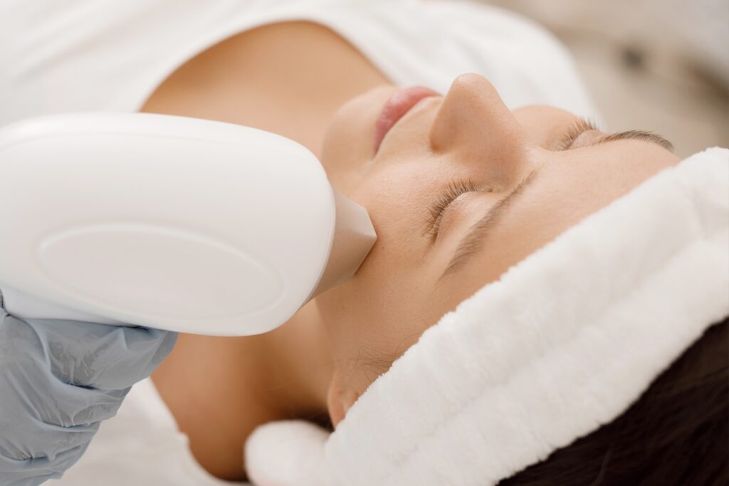 person lying down with eyes closed while an IPL device is placed against their cheek