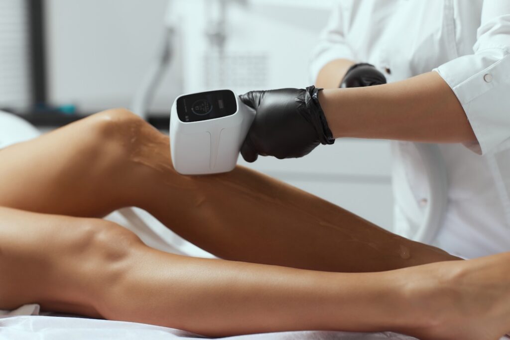 Technician wearing black gloves using a handheld laser device on a woman's lower leg.