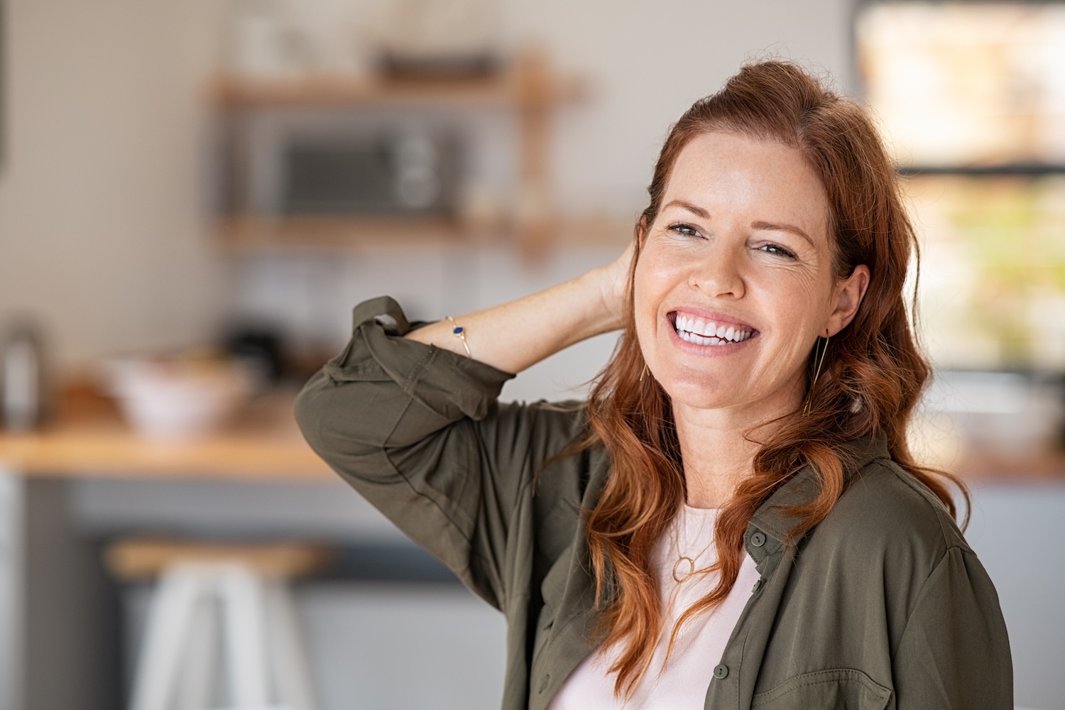 woman with shoulder-length hair smiling indoors, one hand resting behind her head