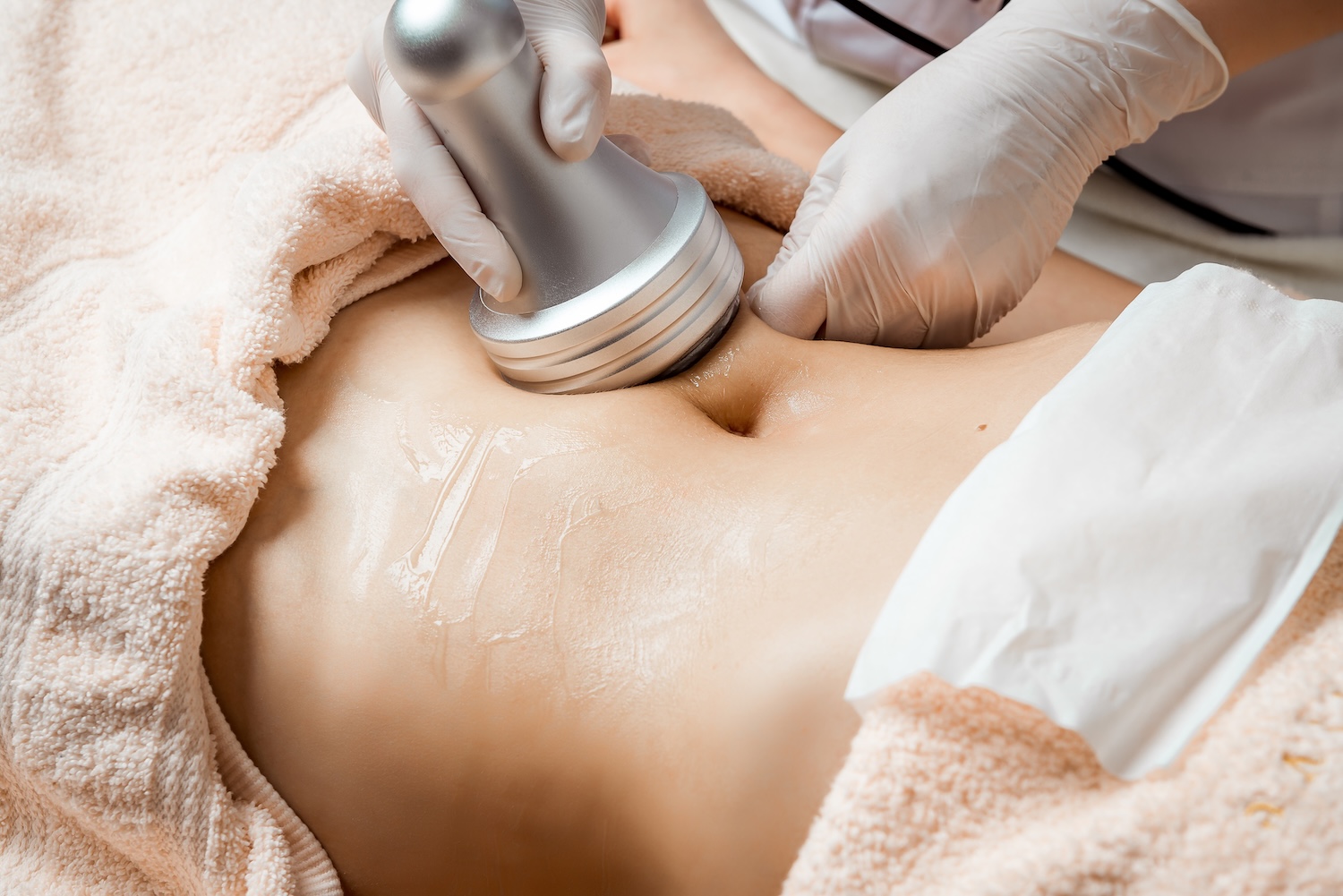 Gloved hands hold a handheld device against the abdomen of a person lying on a treatment table.