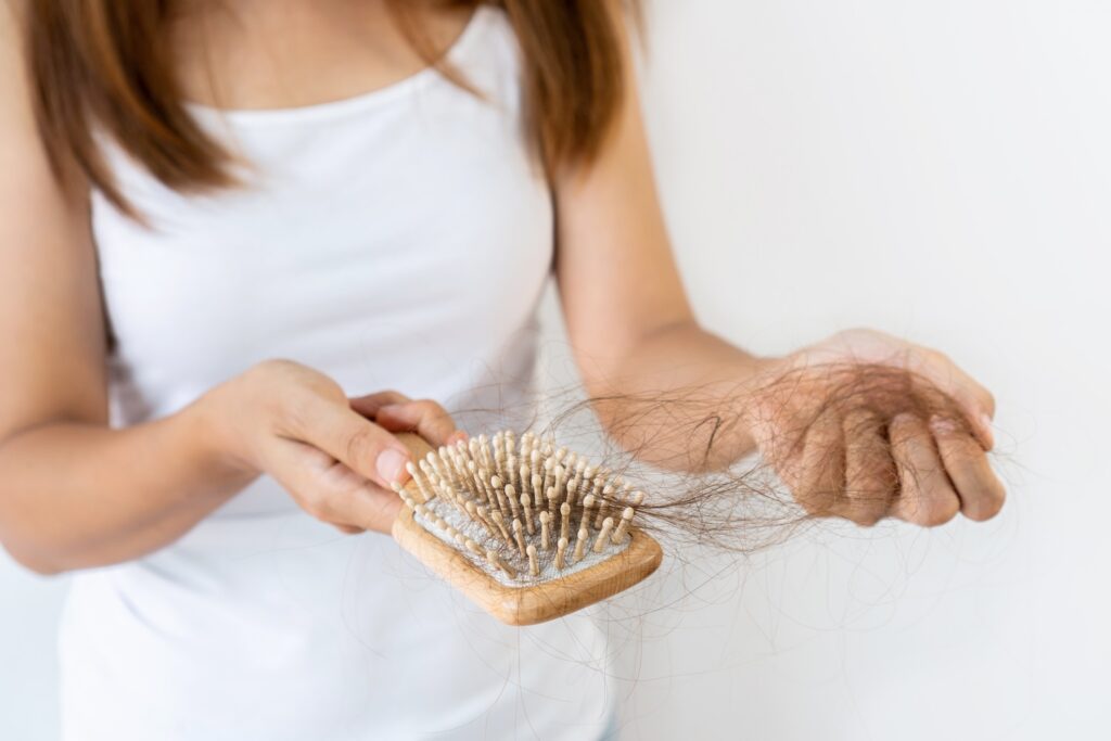 person holding a wooden hairbrush with loose hair strands tangled in the bristles