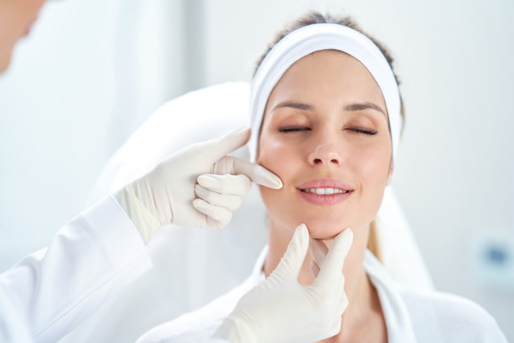 a provider wearing gloves gently assessing a woman's face as she prepares for injectable treatment
