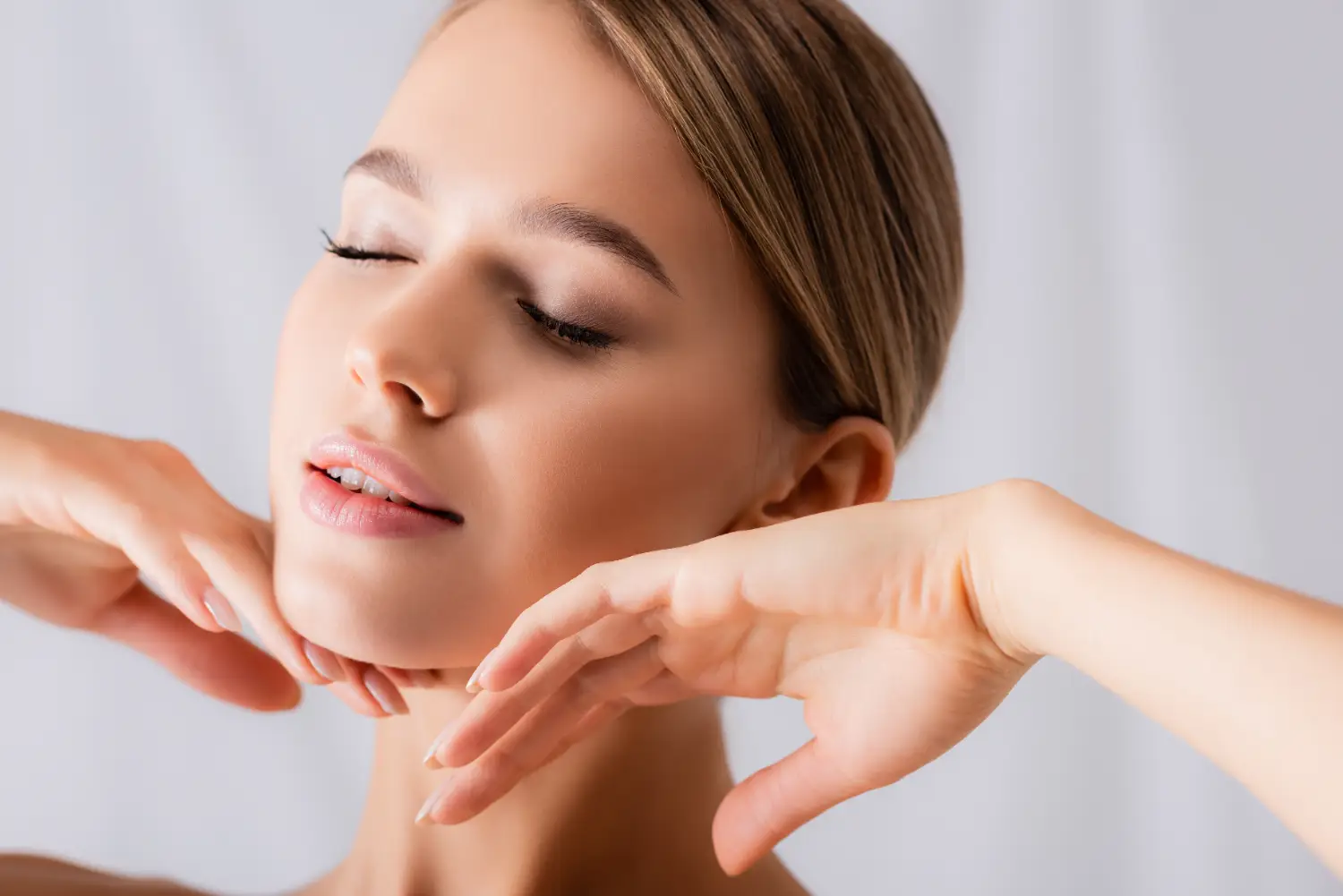 Close-up of a woman with smooth, radiant skin gently framing her face with her hands.