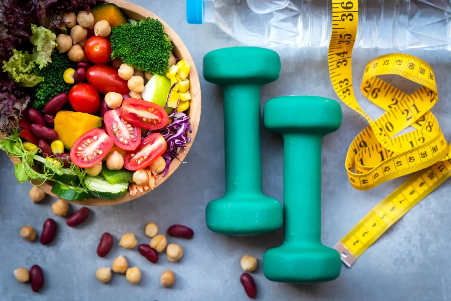 Healthy salad bowl, green dumbbells, measuring tape, and water bottle arranged on a table.