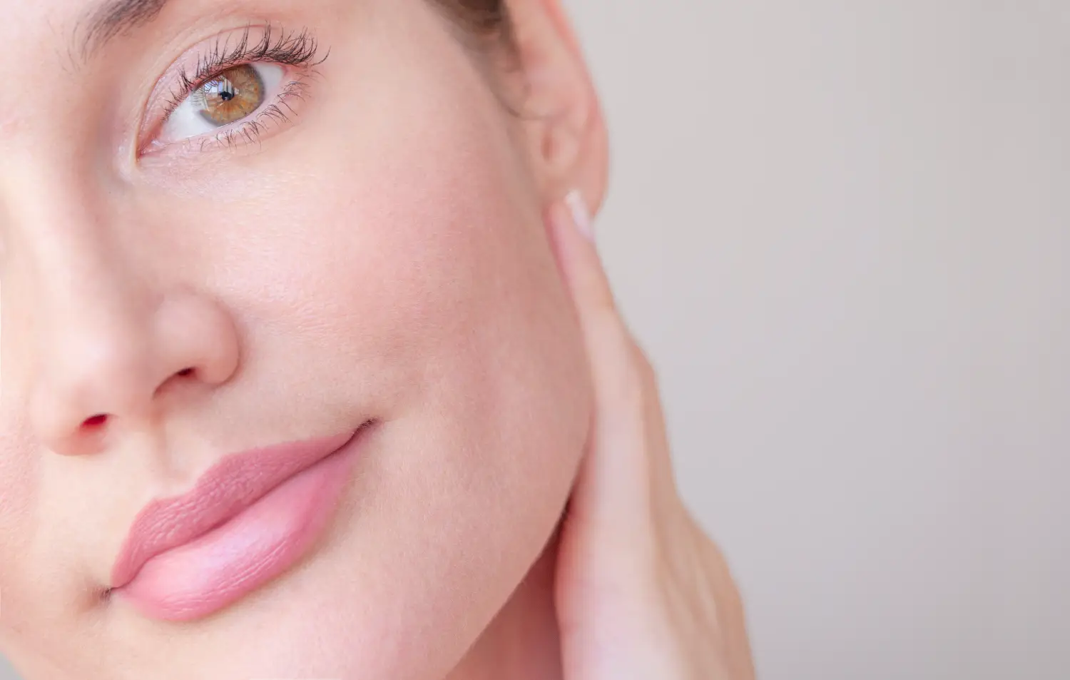 Close-up of a woman’s face showing her cheek, lips, and one eye while her hand rests along her jawline.