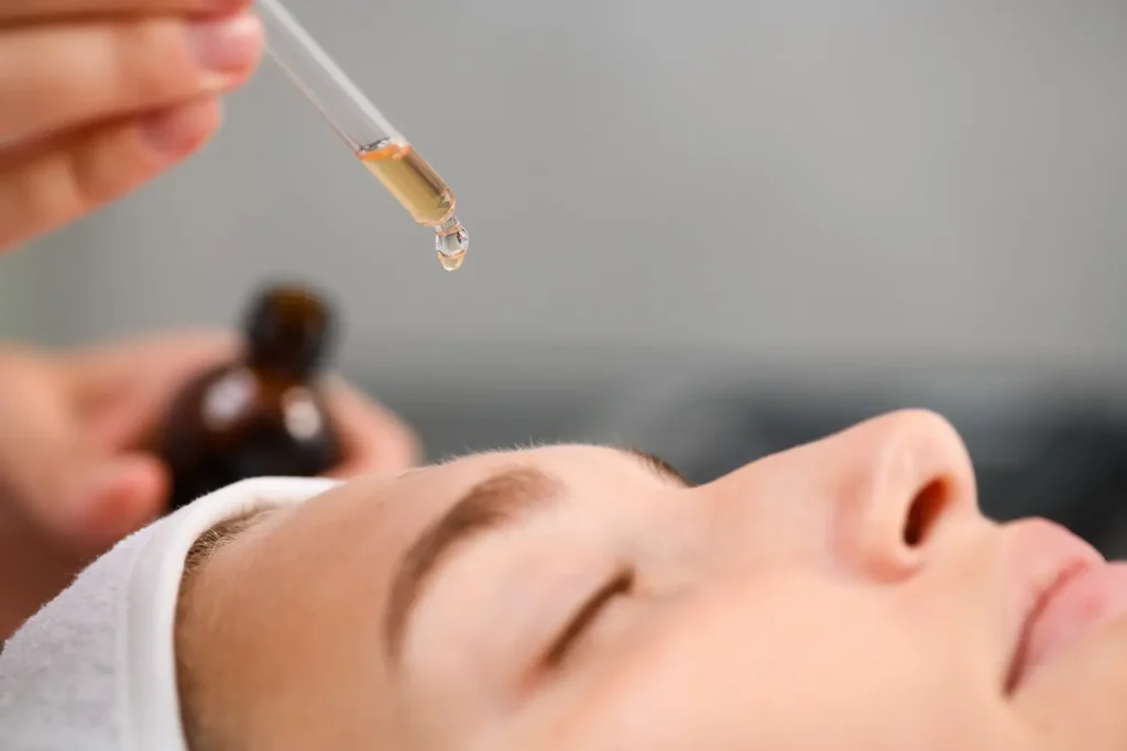 Dropper holding a clear liquid positioned above a person’s forehead as they lie down with eyes closed