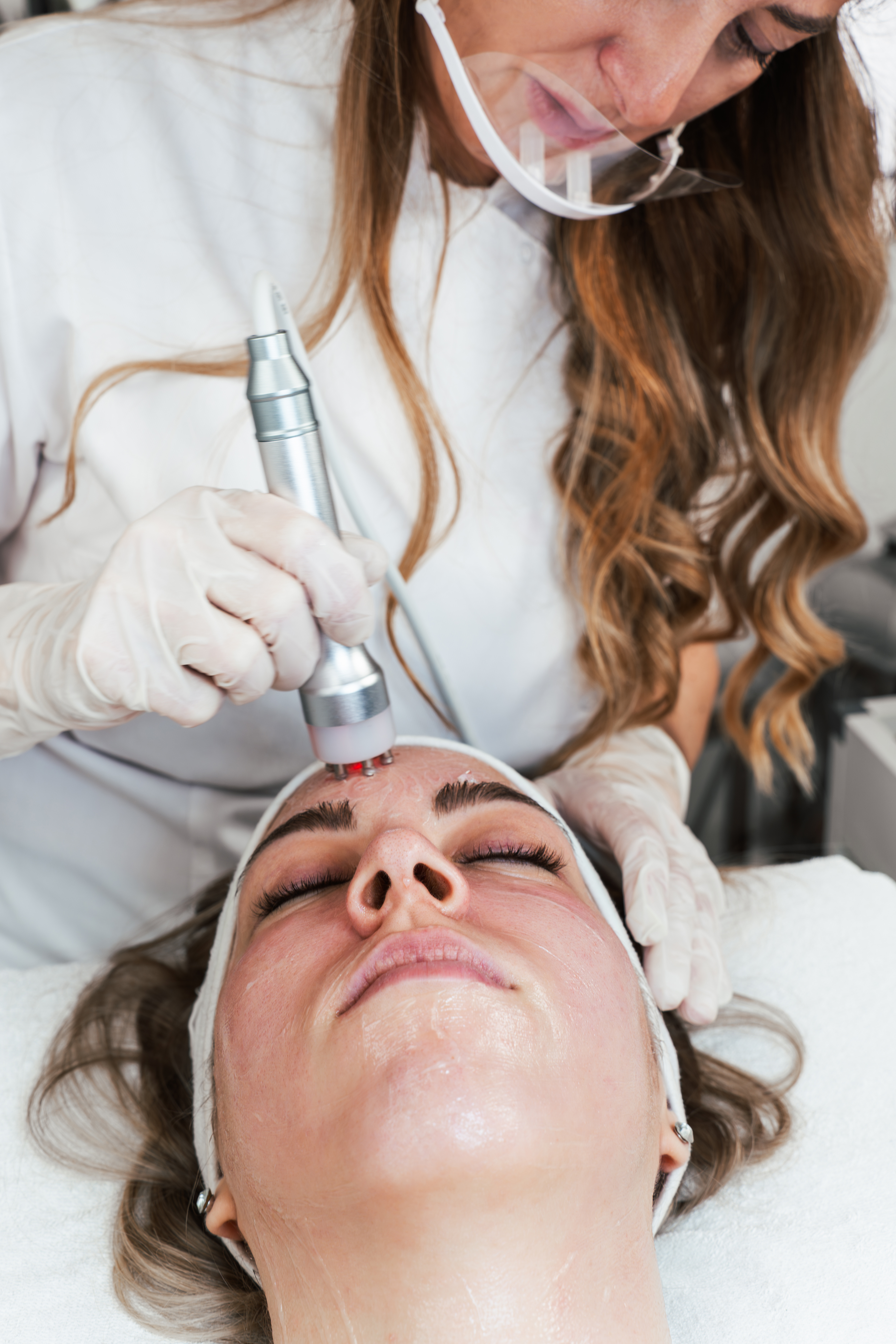 Practitioner using handheld device on woman’s face during skin treatment