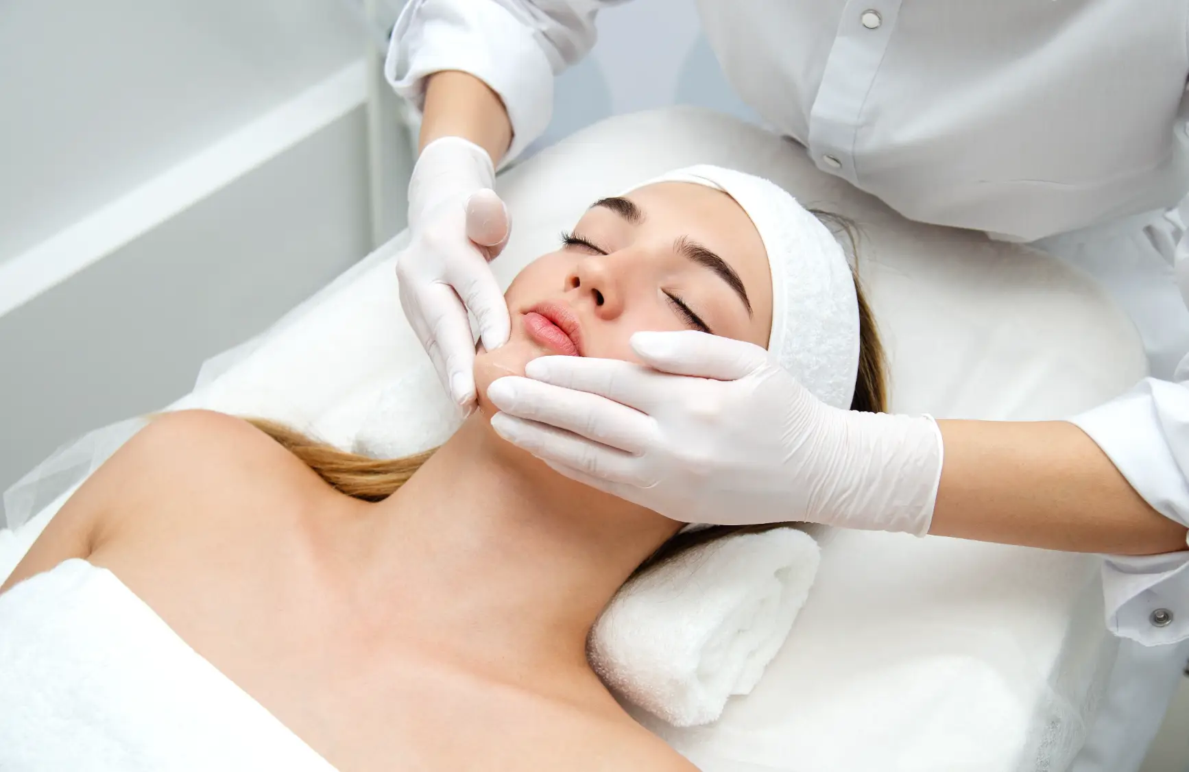 Practitioner wearing gloves performing a facial treatment on a relaxed woman