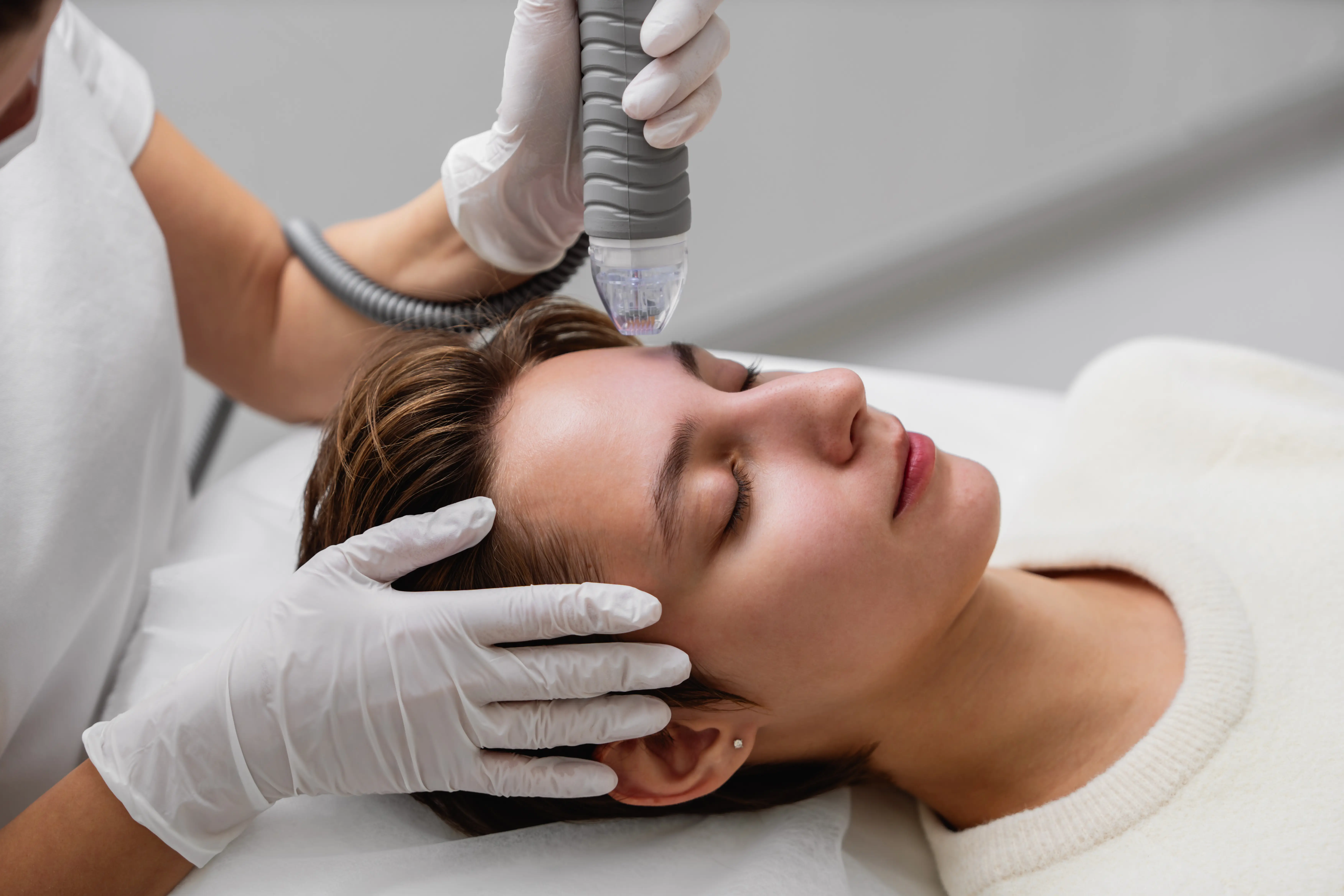 Close-up of microneedling device applied to woman’s forehead by gloved hands