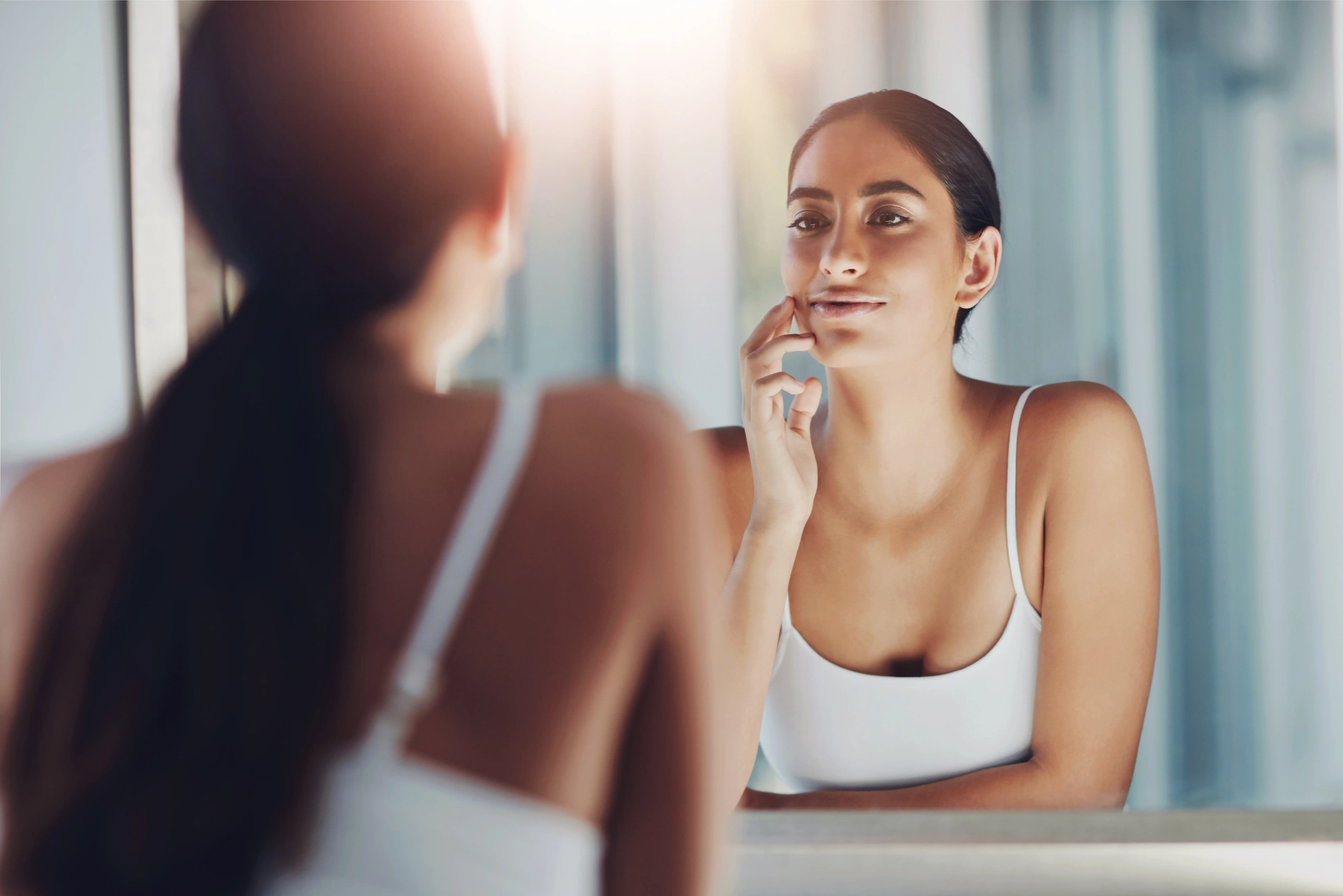 Woman touching her cheek while looking in mirror with soft lighting