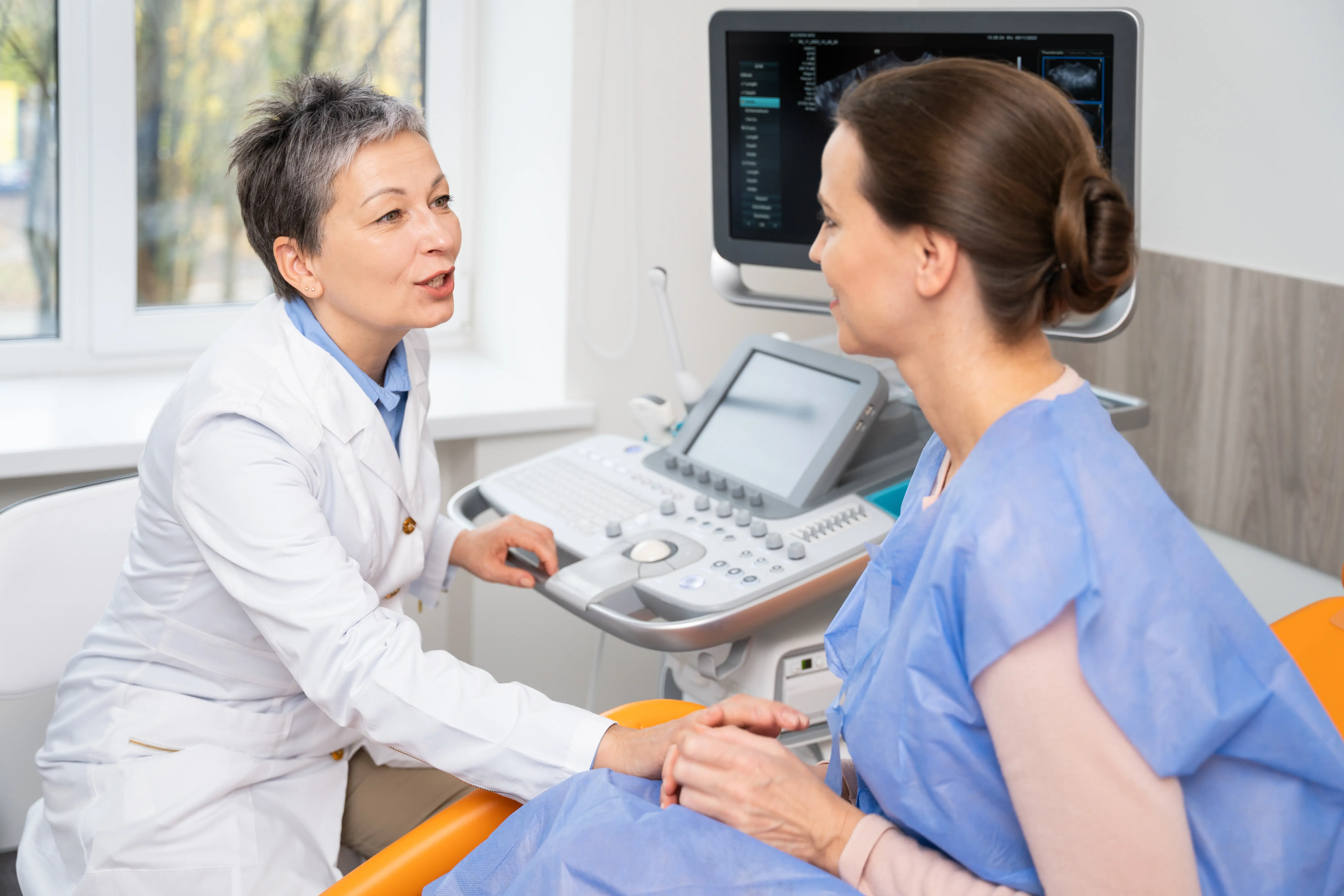 Healthcare provider consulting with woman in exam room beside medical imaging equipment