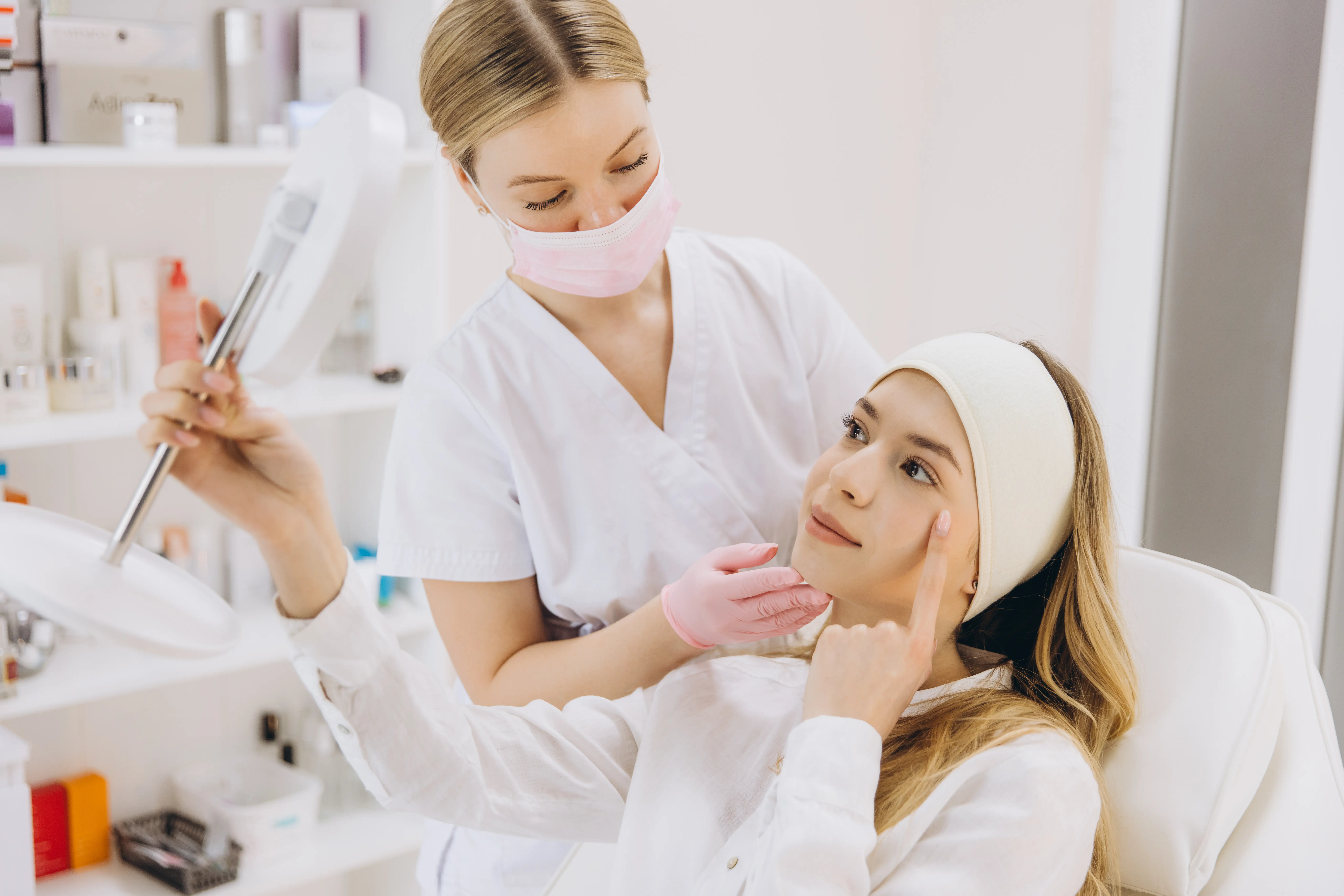 Client looking in a mirror while a skincare professional examines her face