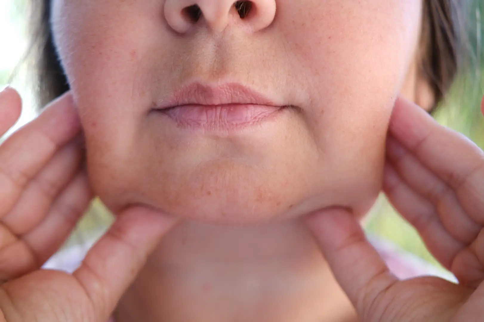 Close-up of a woman holding the skin beneath her jaw with both hands.
