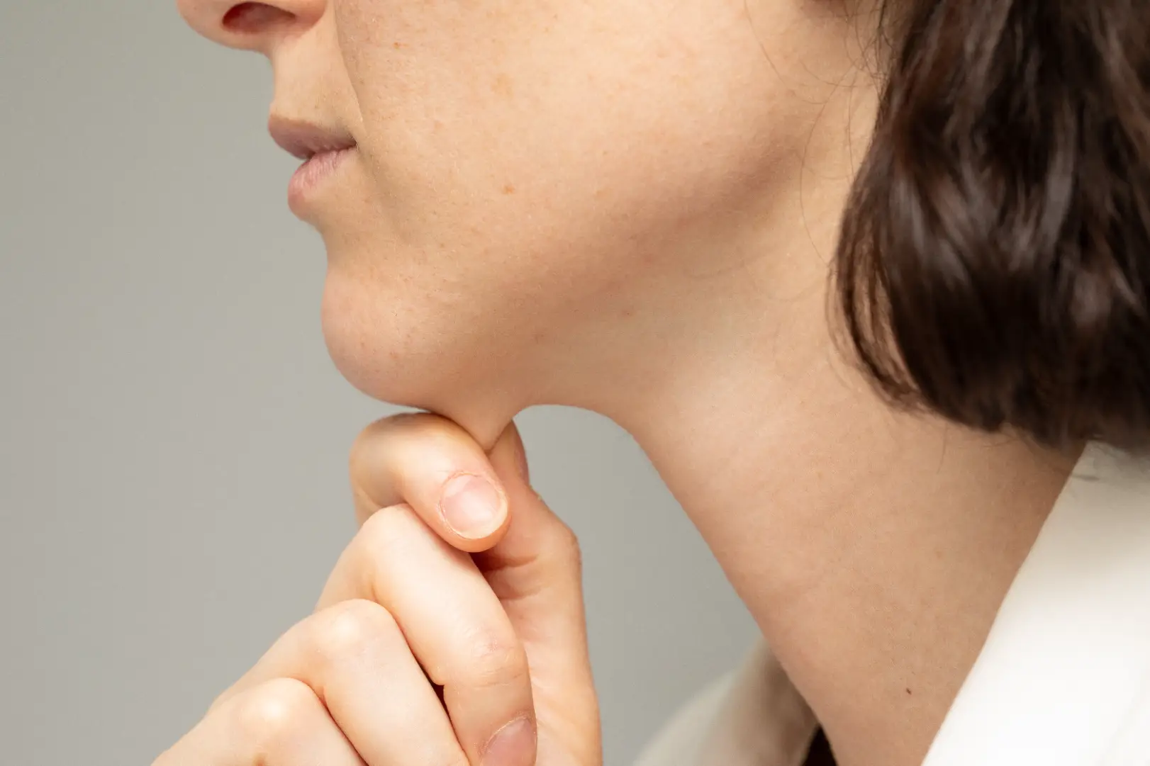 Side view of a woman pressing a finger beneath her chin along the jawline.